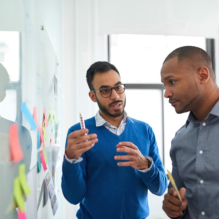 Two people meeting in an office, looking at post-it notes on a whiteboard