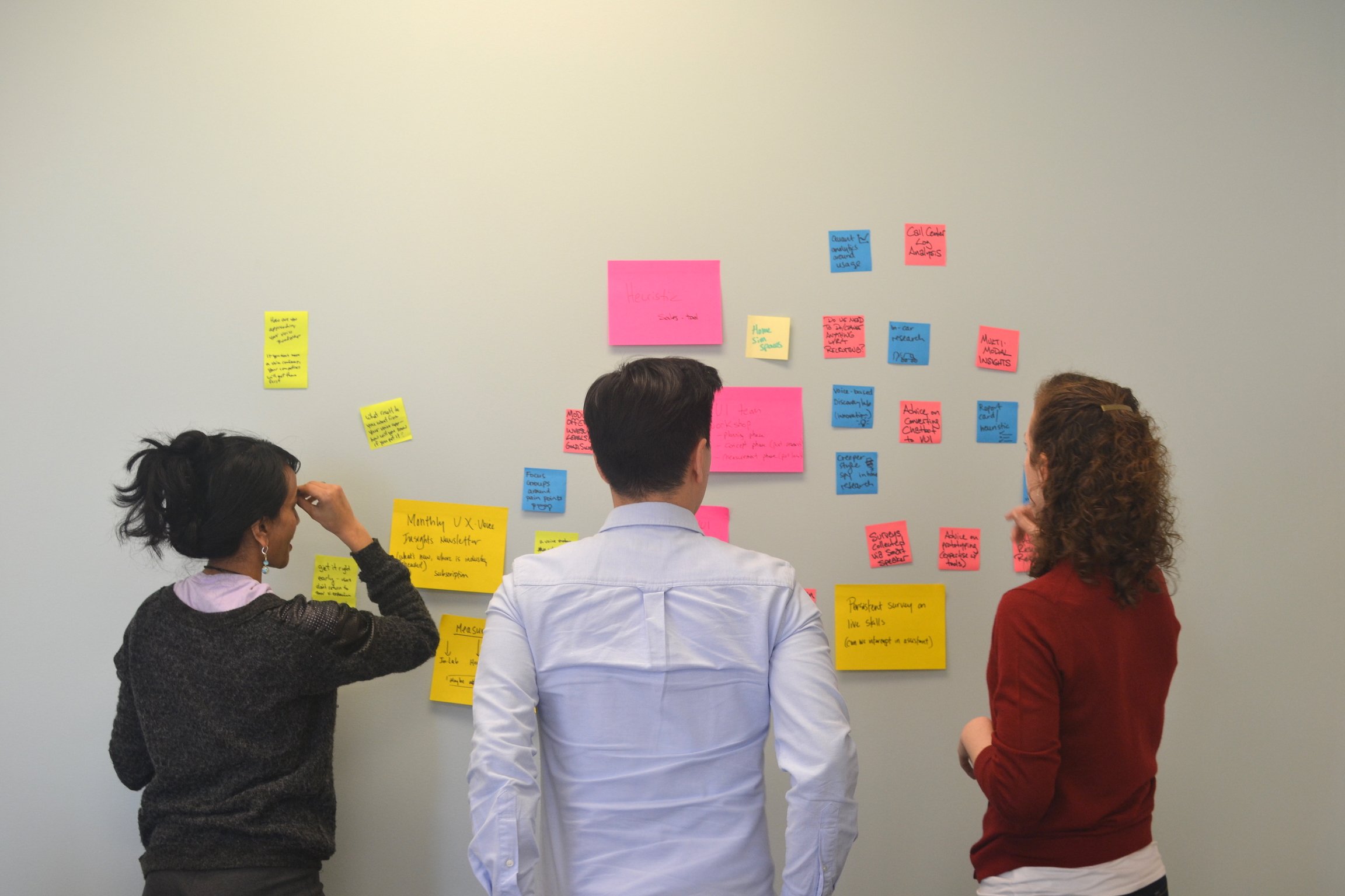 Two women and one man putting sticky notes on a wall Two women and one man putting sticky notes on a wall