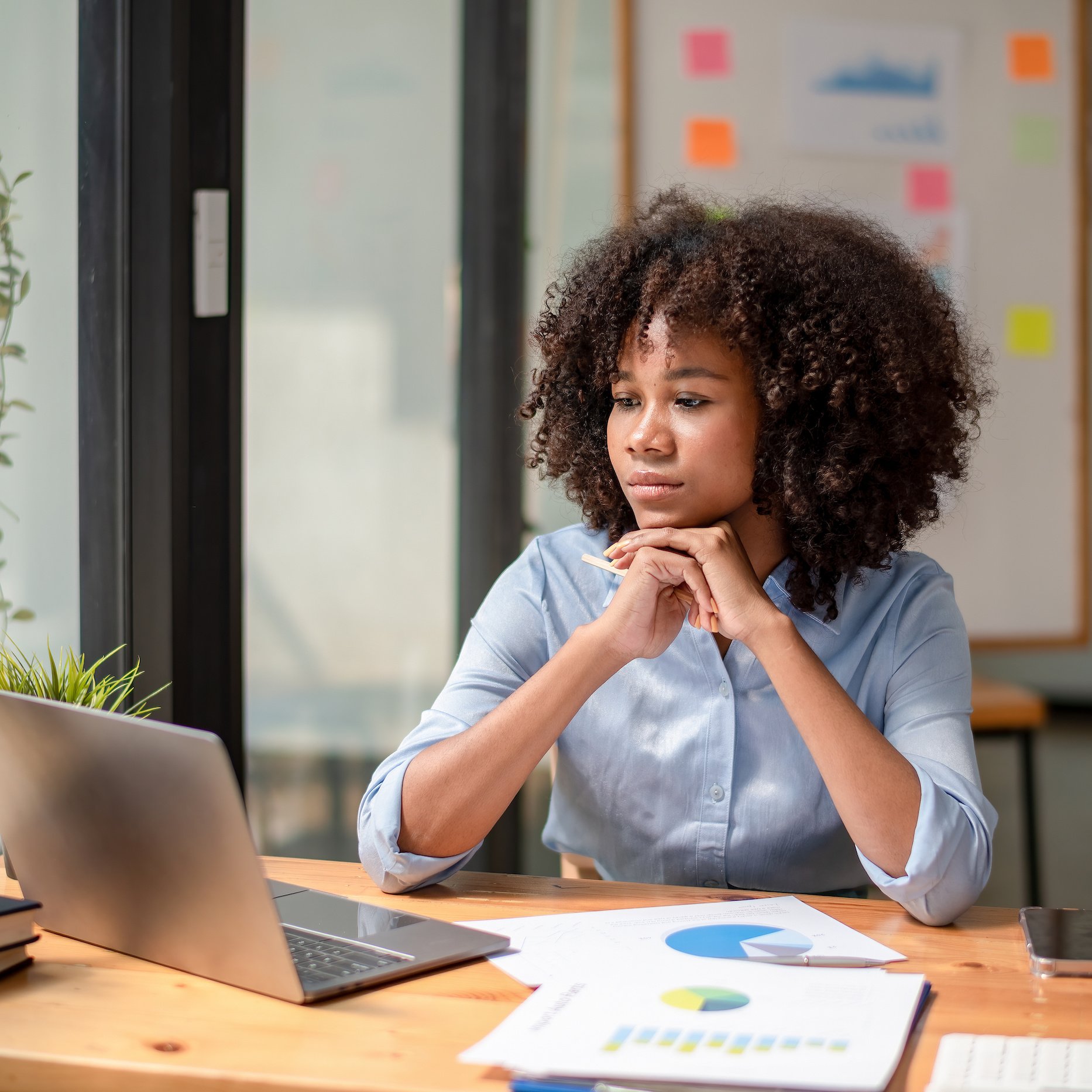 Woman sitting at her desk in front of laptop with sticky notes and charts in the background