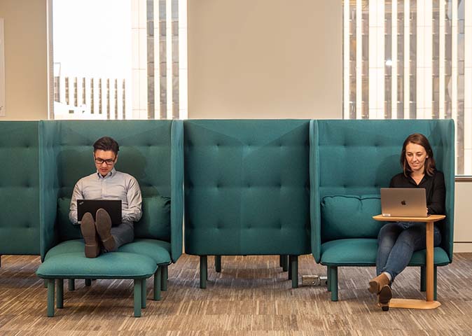 Two people sitting at large cozy desk spaces working on laptops