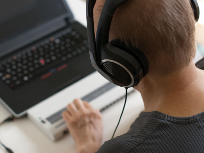 Man with headphones using a braille reader with his laptop