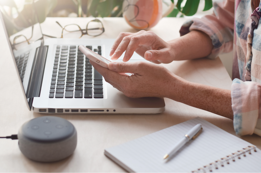 Set of hands using a mobile phone with laptop and Amazon Alexa in the background