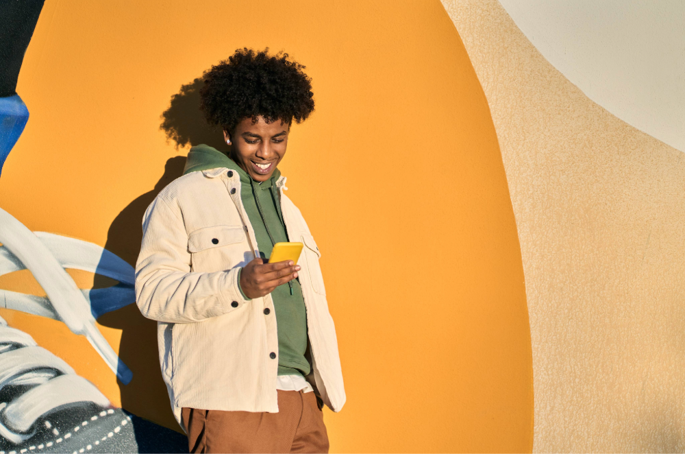 Young man standing against bright orange wall looking at smart phone