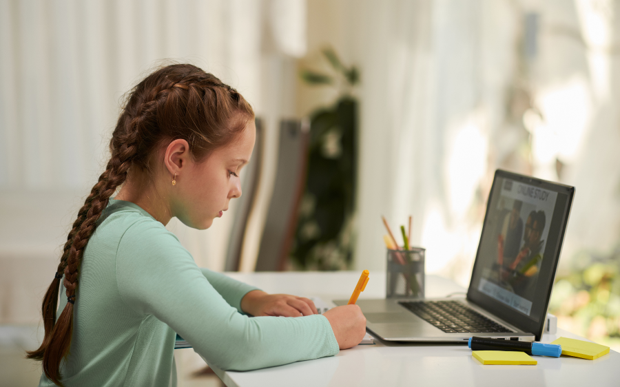 Young girl doing homework at her desk in front of a laptop