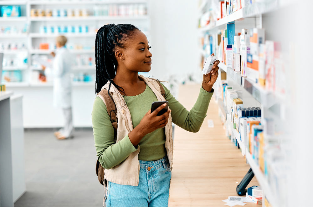 woman in pharmacy looking at medicine and her phone