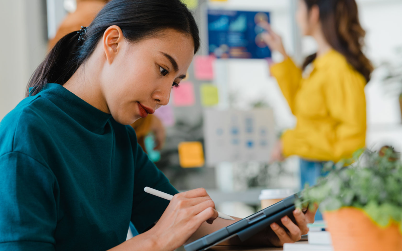 Woman working on tablet with sticky notes and brainstorming wall in the background